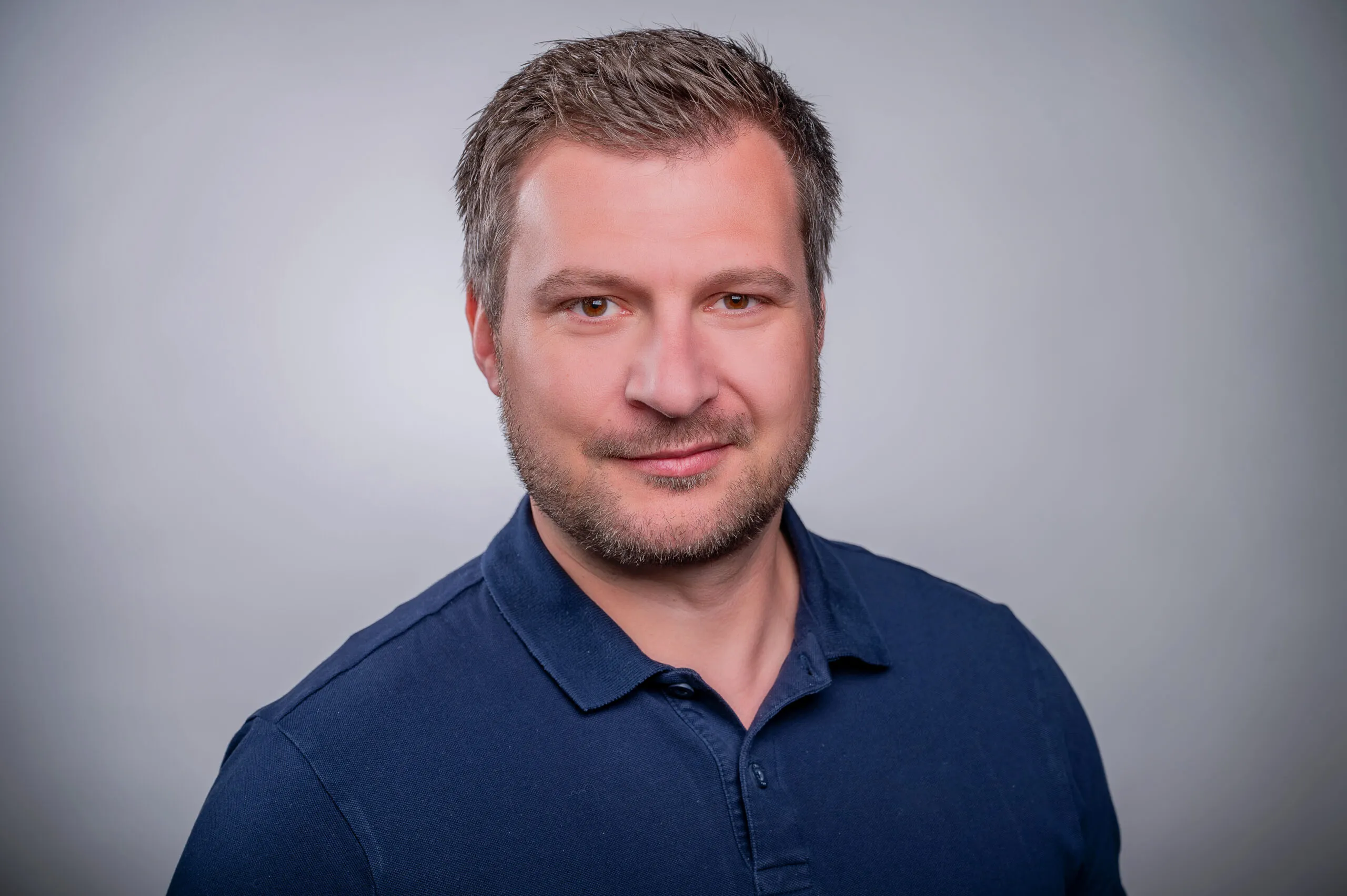 Porträt von Michael Zabel. Er trägt ein blaues Polohemd, der Hintergrund ist grau.
